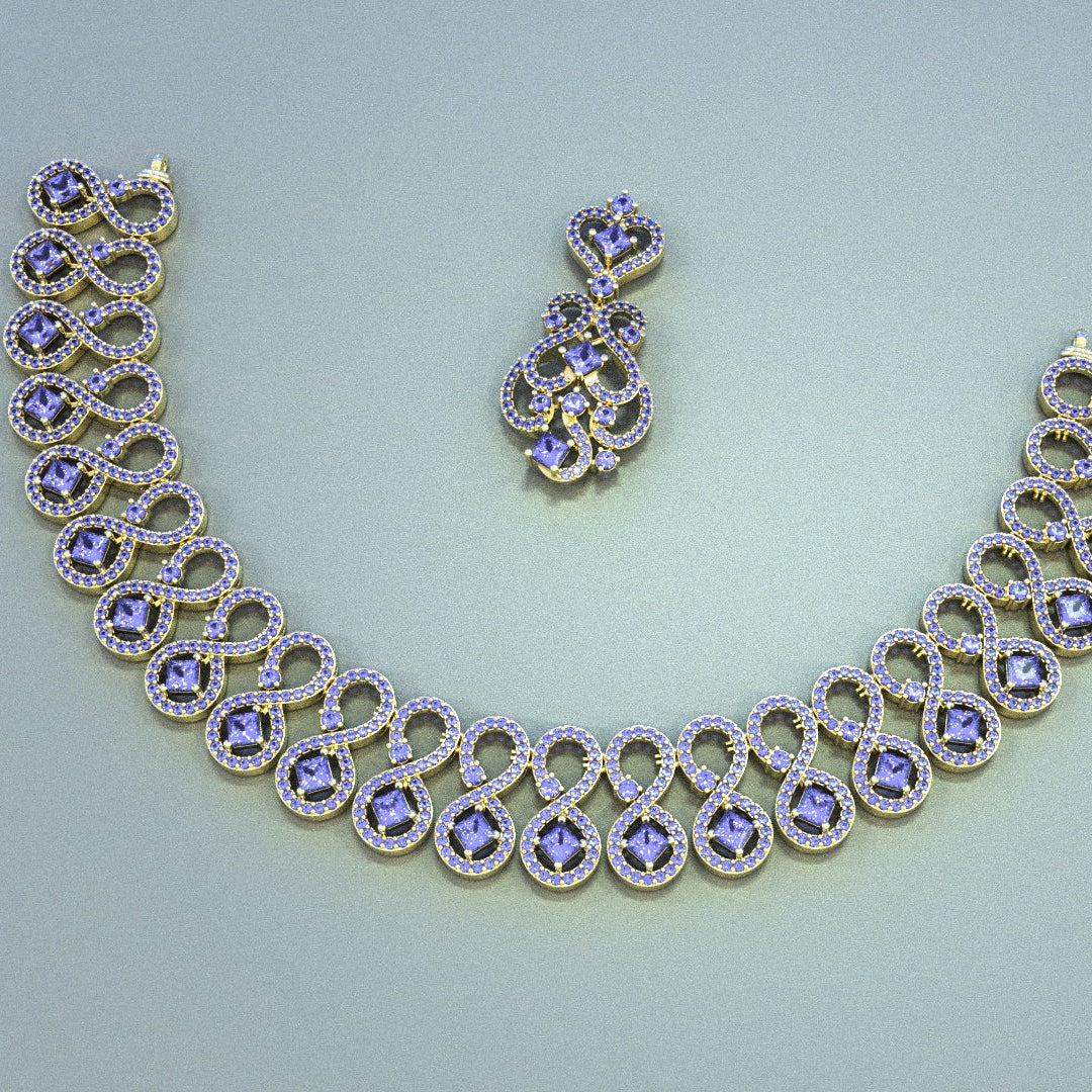 Gold-toned jewelry set featuring an ornate chain necklace and matching drop earrings, both decorated with small clear stones and central lavender-purple flower-shaped stones, displayed on a light gray background.