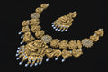 Gold necklace with intricate designs and blue stones on a black background