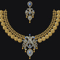 An ornate gold-toned traditional necklace set with matching earrings, featuring circular coin-like motifs along the shoulders and blue stone accents, displayed on a solid black background.