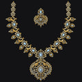 An ornate gold-toned jewelry set featuring a necklace and matching earrings, embellished with light blue stones and small clear stones, displayed on a solid black background.