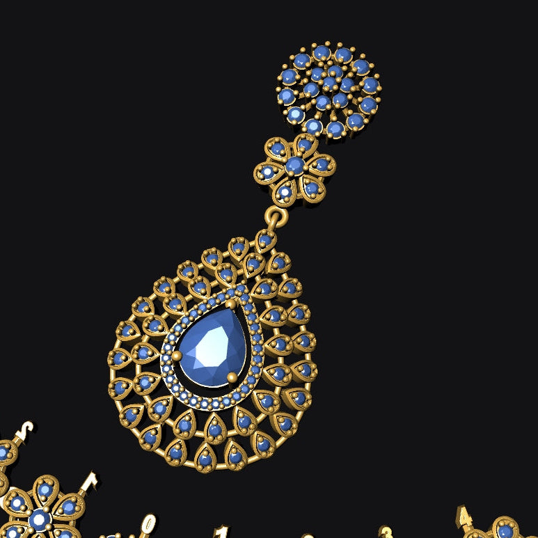 An ornate gold-toned jewelry set with deep blue gemstones, featuring a teardrop pendant with a central blue stone and matching floral motifs, shown against a solid black background.