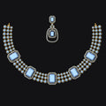 Gold-plated statement necklace and matching drop earring set with light blue rectangular gemstones and small clear stones, displayed on a solid black background.