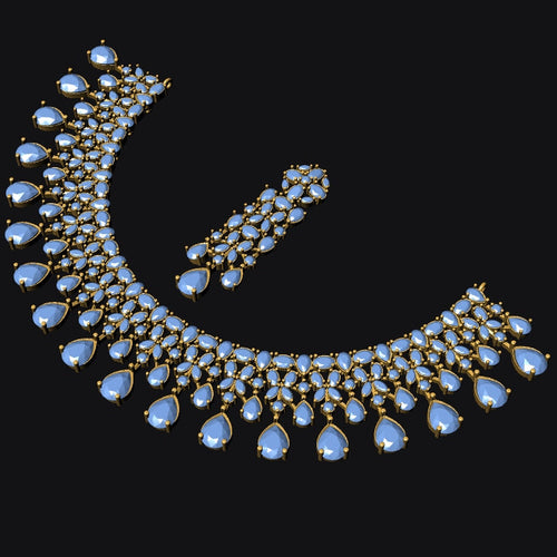 A gold-toned crescent-shaped statement necklace with matching drop earrings, featuring light blue teardrop-shaped gemstones and clear stones, set against a solid black background.