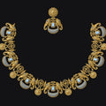 An ornate gold-toned jewelry set featuring a necklace and matching earring, decorated with intricate scrollwork, floral motifs, and oval blue-and-white stone inlays, displayed against a solid black background.