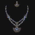 An ornate gold-toned double-strand necklace with a matching stud earring, featuring light blue stones and gold accents, displayed against a solid black background.