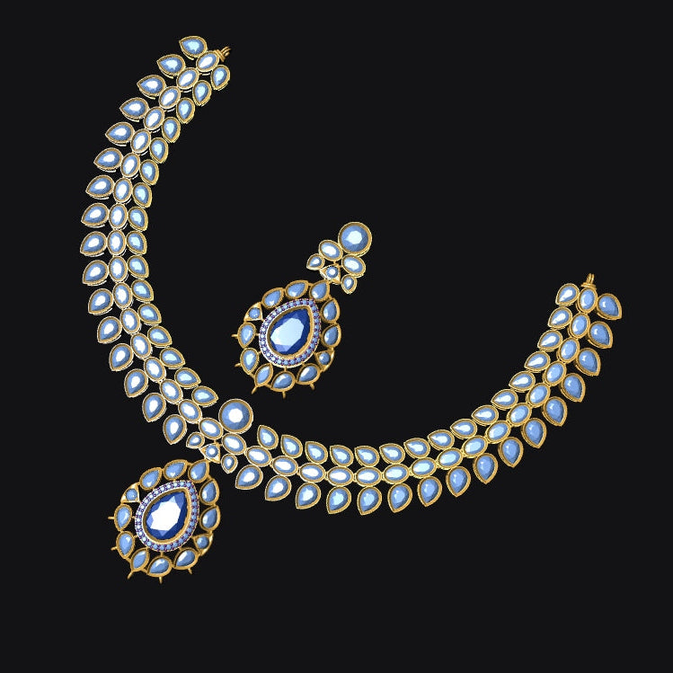 Gold-plated traditional Indian jewelry set featuring a curved necklace with white stones, a matching pendant, and a teardrop earring, accented with blue stones, set against a solid black background.