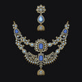 An ornate gold-toned traditional necklace set with blue stones and white stones, shown against a solid black background.